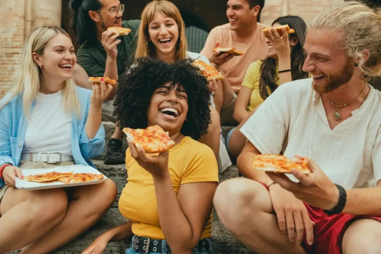 People enjoying delicious Italian pizza in a group, laughing and talking together. A perfect example of food, gastronomy, lunch, dinner, dining with friends, and social meetups through HobiZo.